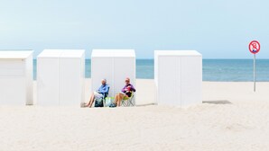 Ein Strand mit weißen Strandhütten und einem Verbotsschild für parkende Autos.