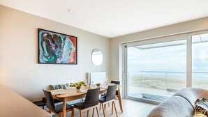 Ein modernes Wohnzimmer mit Essbereich, einem großen abstrakten Gemälde und einem Balkon mit Blick auf den Strand.