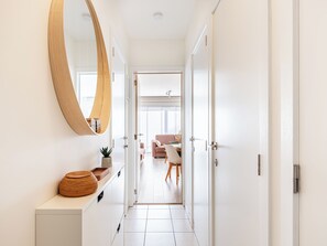 A hallway with a round mirror, a wooden cabinet, and a potted plant. - Nicely equipped flat with prime location (Koksijde)