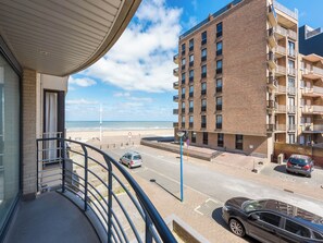 En balkon med udsigt over en strand, hvor man kan se en høj bygning og parkerede biler.