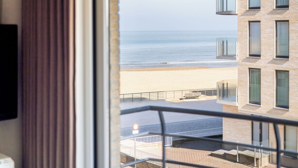 A window view of a beach with a building in the background.