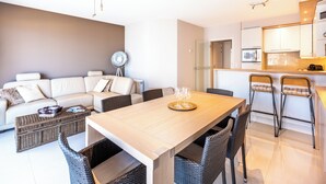 A modern living room with a sofa, a dining table, wicker chairs, a fan, and a kitchen area with a microwave and cabinets.