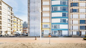 A multi-story building with a mix of residential and commercial spaces, including a visible entrance with a door and windows. - Cosy family flat with sea view (Koksijde)