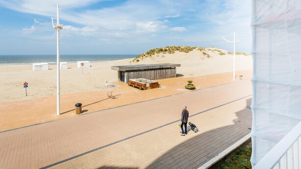 A beachside walkway with a wooden structure, a trash bin, and a no parking sign. - Cosy family flat with sea view (Koksijde)