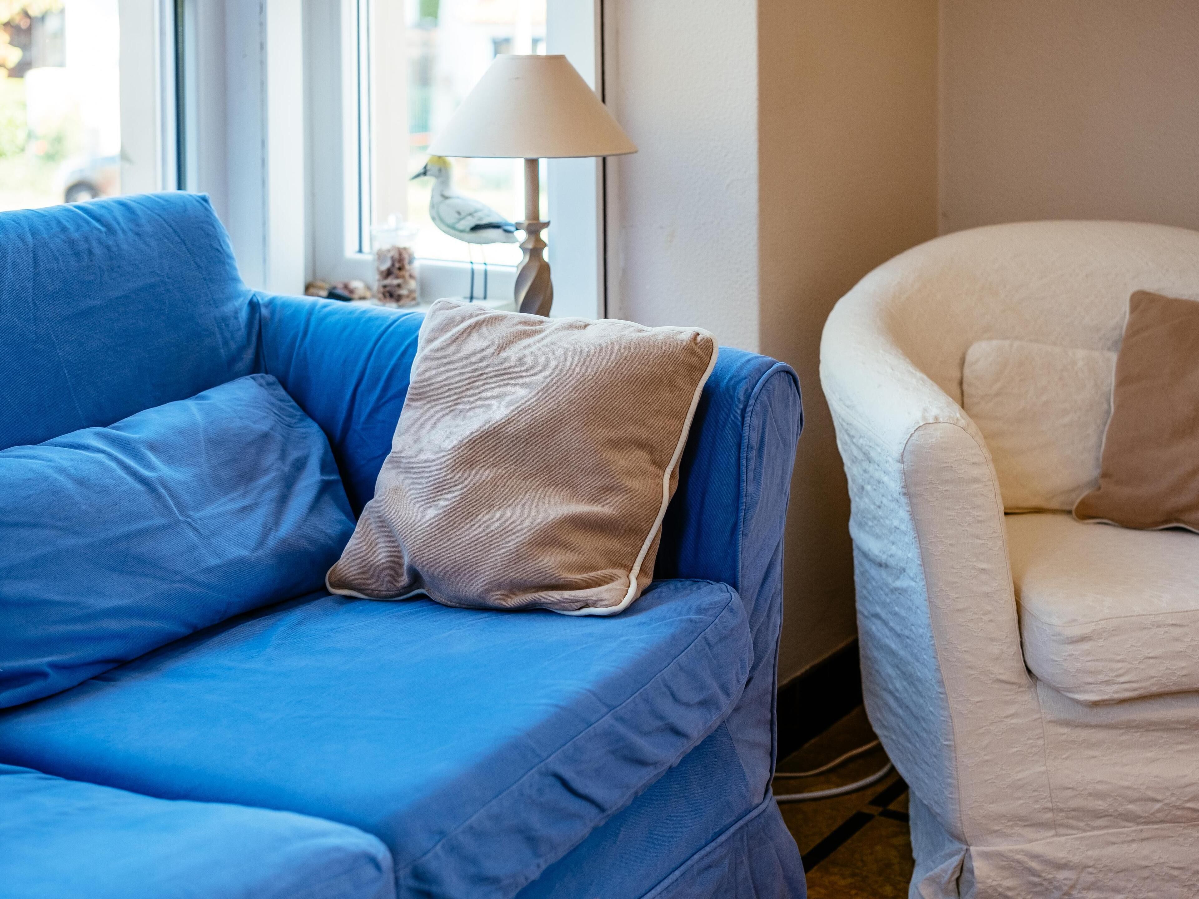 Un canapé bleu avec un coussin beige et un fauteuil blanc avec un coussin beige.
