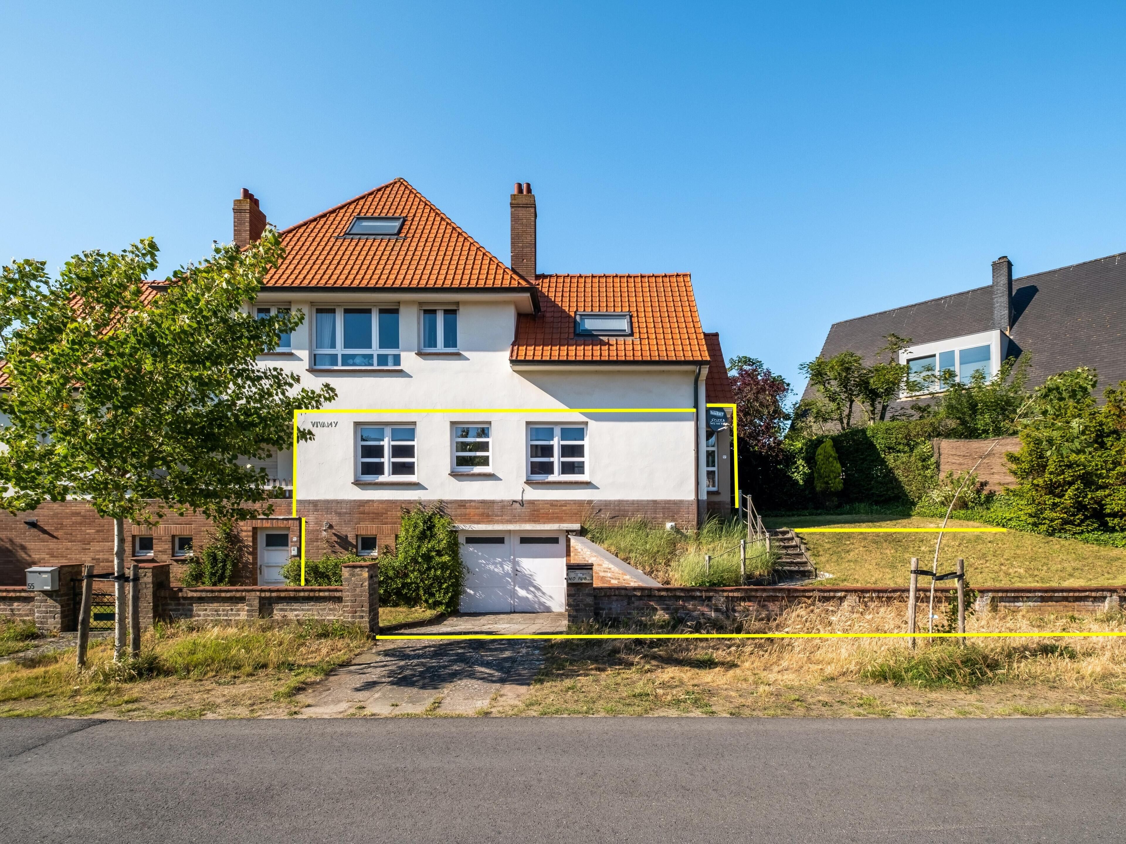 Une maison à deux étages avec un toit recouvert de tuiles rouges, un garage et une cour avant délimitée par une ligne jaune.