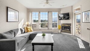 Ein Wohnzimmer mit grauem Sofa, einem weißen Couchtisch, einem Kamin und großen Fenstern.