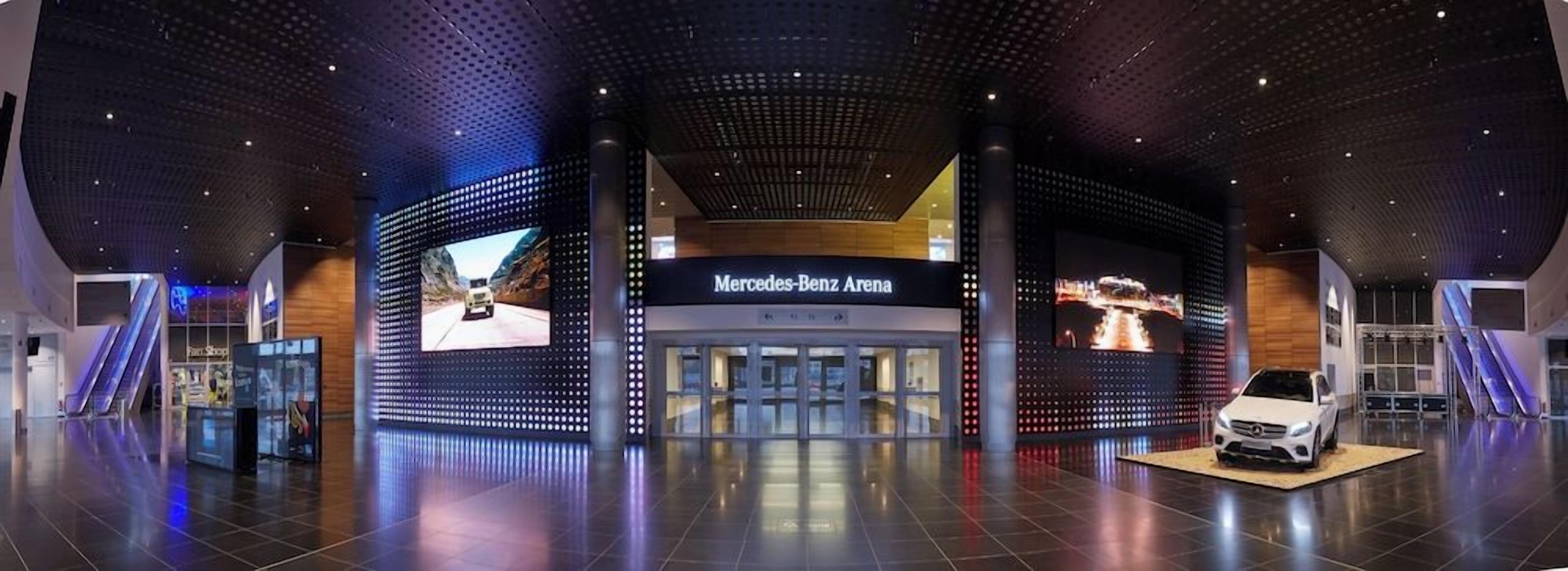 A modern Mercedes-Benz Arena with a large digital display, a car exhibit, and a spacious interior.