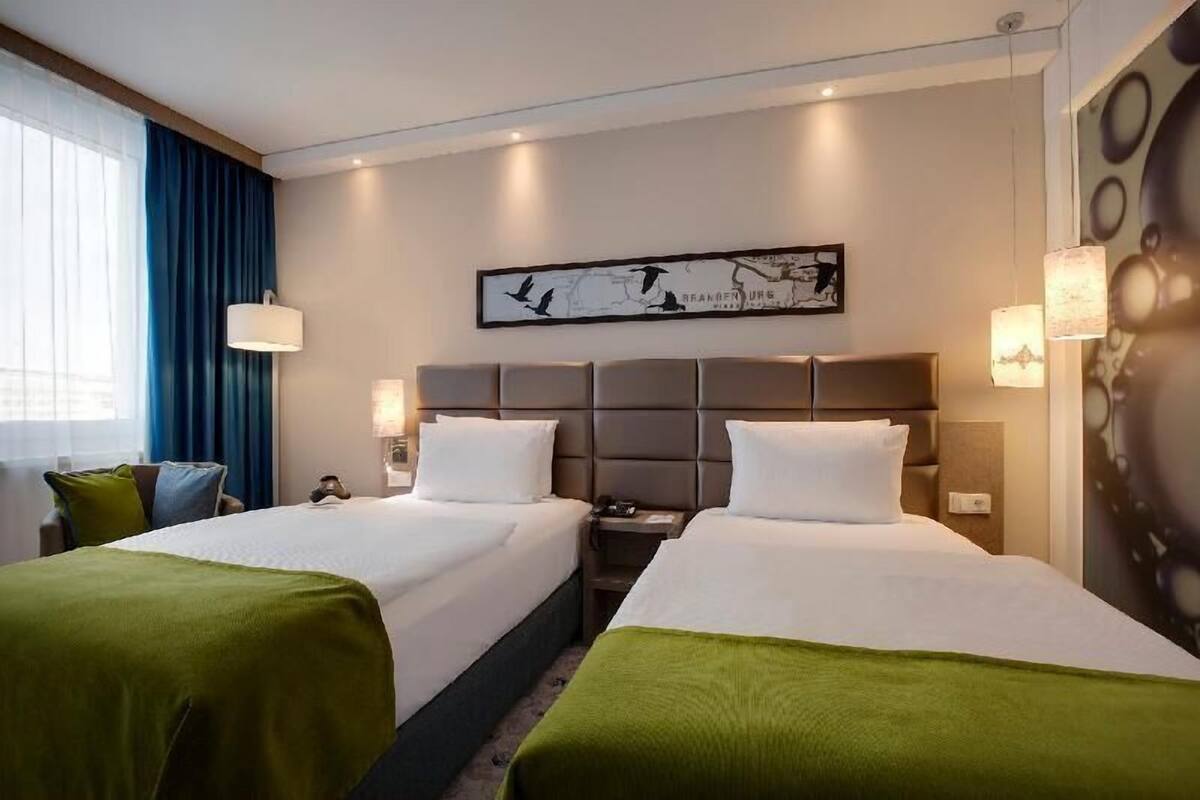 A hotel room with two beds, a map artwork on the wall, and a window with curtains.