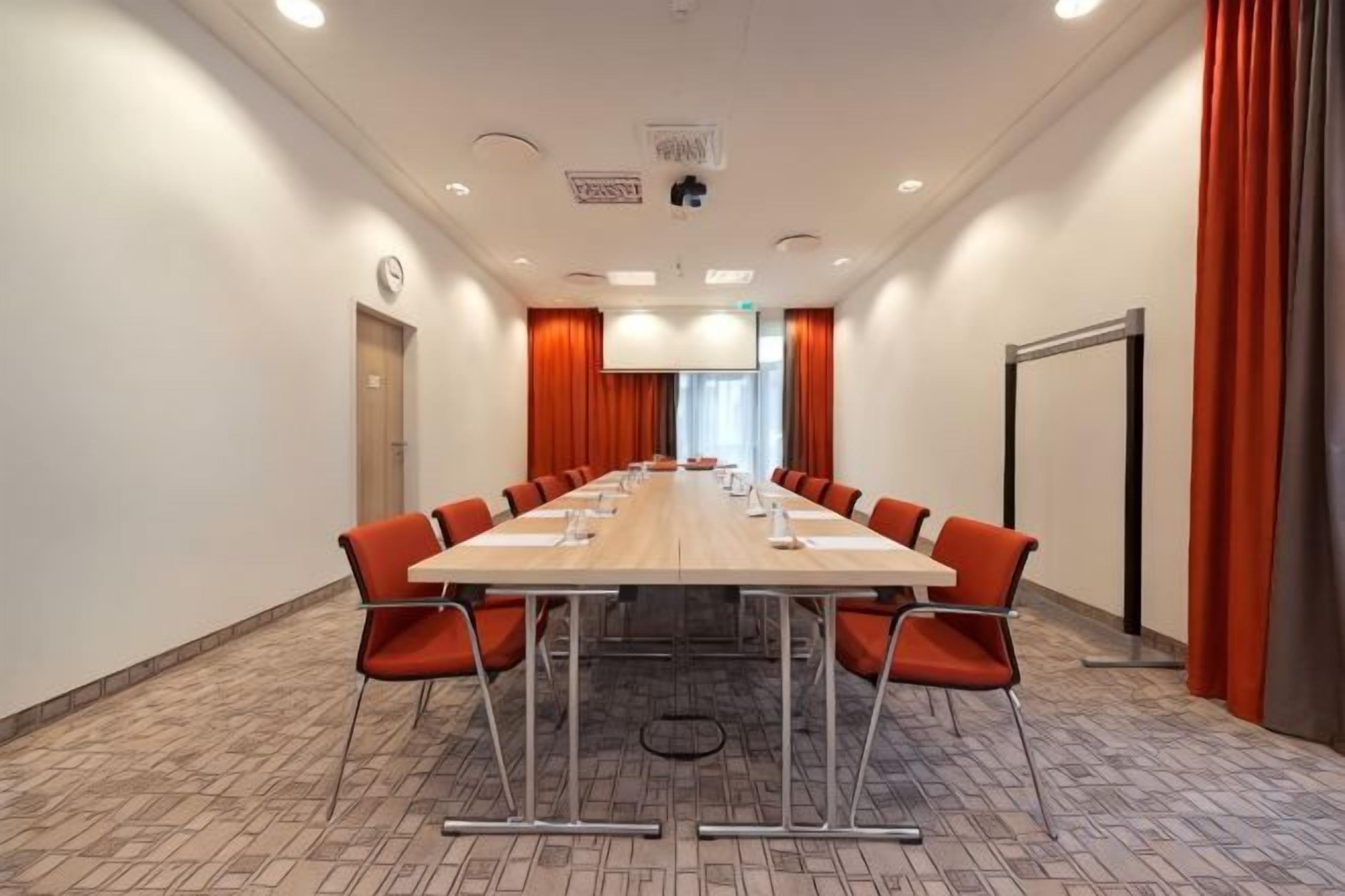 A conference room with a long table, chairs, and a projector screen.