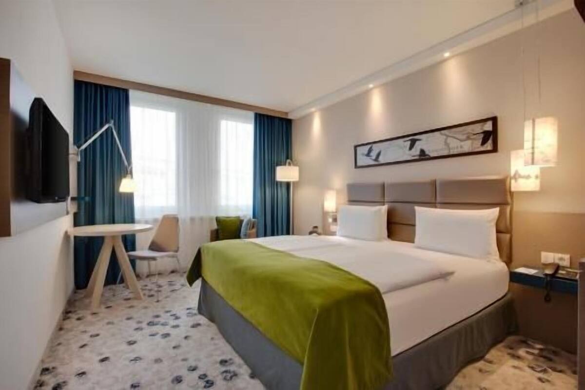 A hotel room with a bed, bedside tables, a desk, a chair, and a television.