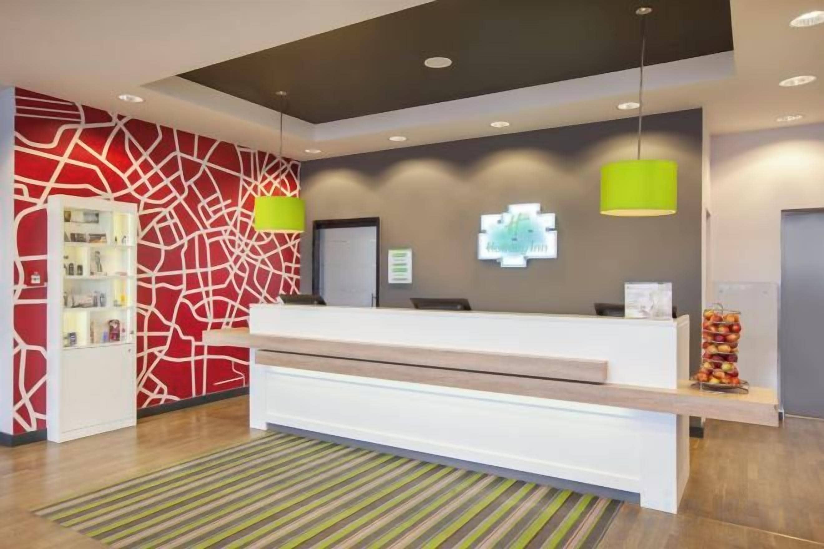 A reception area with a white reception desk, a red abstract wall, and a green pendant light.