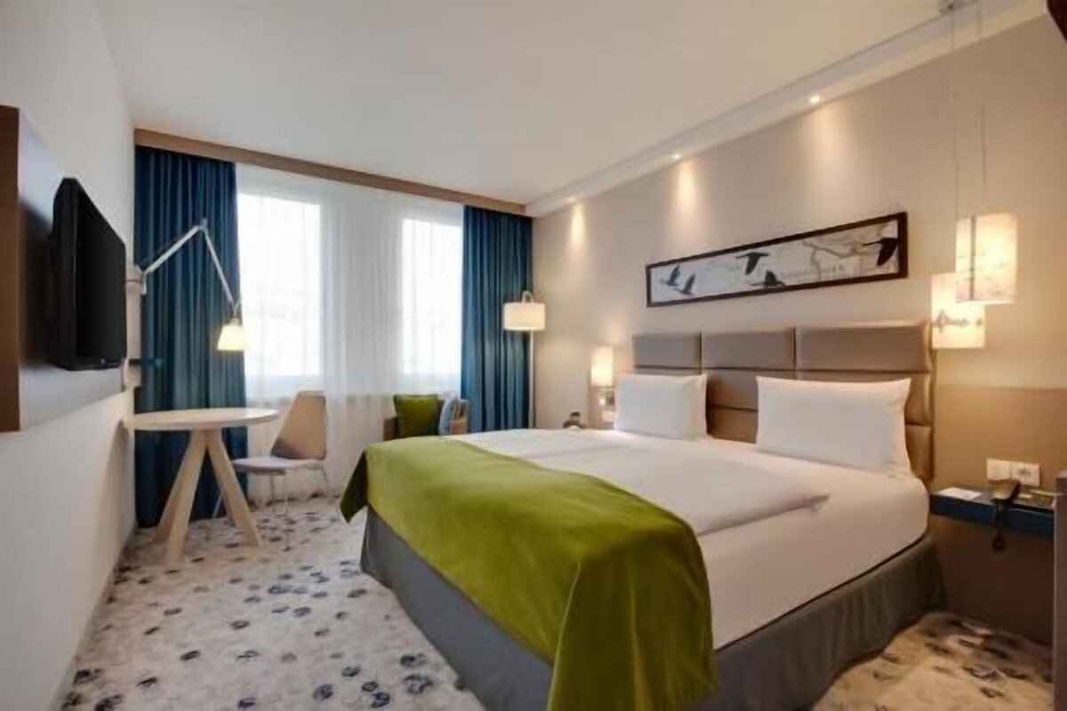 A hotel room with a bed, bedside tables, a desk, a chair, and a television.