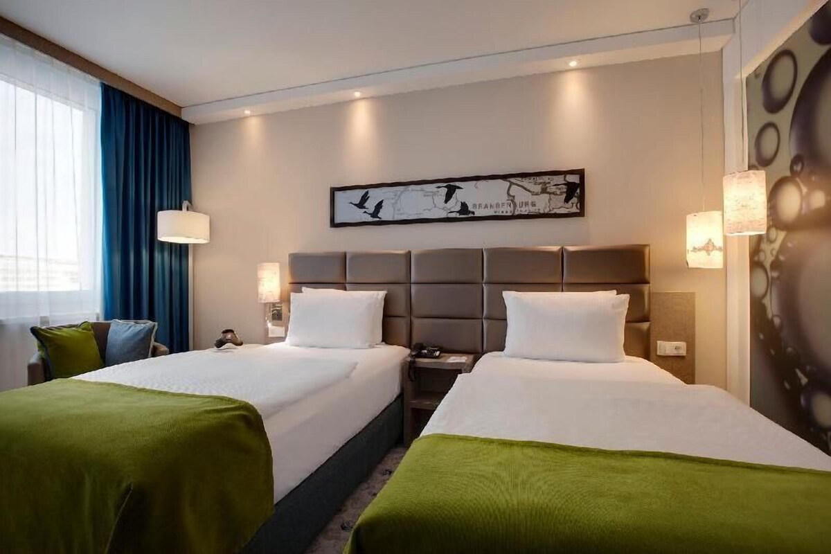 A hotel room with two beds, a map artwork on the wall, and a window with curtains.