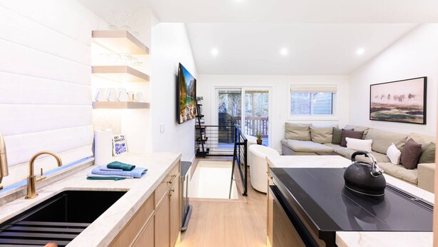 A compact kitchen with a sink, countertop, and a dining area with a black stove top. A staircase leads to a balcony with a view of trees. - Labor Day Sale - Limited Time Offer, Save up to 30% (Park City)