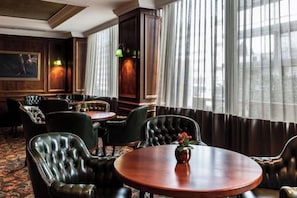 A room with leather chairs, a round table, and a view through large windows. - NJV Athens Plaza (Athens)