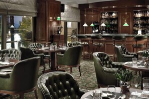 A bar area with leather chairs, a bar counter, and a view of the outdoors. - NJV Athens Plaza (Athens)