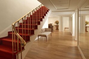 A staircase with a red carpet and golden railings leading to a room with a wooden floor. - NJV Athens Plaza (Athens)