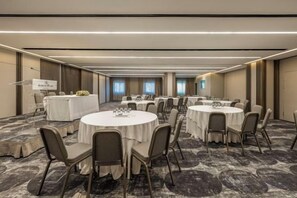 A conference room with multiple round tables, each surrounded by chairs, and a presentation screen at the front. - NJV Athens Plaza (Athens)