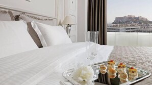A hotel room with a bed, a tray of appetizers, a glass of water, and a view of a historic building. - NJV Athens Plaza (Athens)