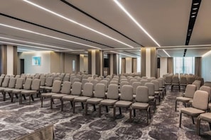 A conference room with rows of chairs, a carpeted floor, and a modern ceiling design. - NJV Athens Plaza (Athens)
