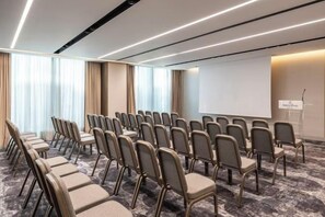 A conference room with rows of chairs, a projector screen, and a presentation podium. - NJV Athens Plaza (Athens)