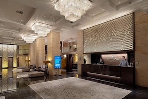 A modern hotel lobby with a reception desk, seating area, and a large chandelier. - NJV Athens Plaza (Athens)