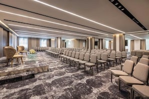 A conference room with rows of chairs, a carpeted floor, and a stage area. - NJV Athens Plaza (Athens)