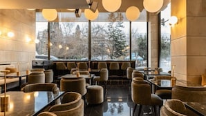 A modern restaurant with a sleek interior, featuring round tables and comfortable seating, large windows offering a view of the outside. - NJV Athens Plaza (Athens)