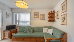 Um quarto aconchegante com um sofá verde, mesa de apoio de madeira e uma televisão sobre um móvel.