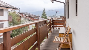 Varanda de madeira com cadeira de madeira e mesa pequena, com vista para uma área residencial com casas e uma grua de construção ao longe.