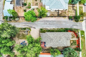 An aerial view of a residential area with a house featuring a sloped roof, a fenced yard, and a paved driveway.
