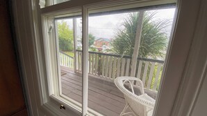 Blick durch ein Fenster mit weißem Rahmen auf ein Holzdeck mit einem weißen Stuhl und einem weißen Geländer.