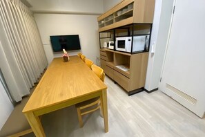 A dining area with a wooden table and chairs, a television mounted on the wall, and built-in shelving with kitchen appliances. - Core Royal-Vacation Rental (Kyoto)