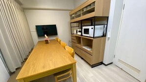 A modern room with a wooden dining table, yellow chairs, a flat-screen TV, and built-in shelves with appliances. - Core Royal-Vacation Rental (Kyoto)