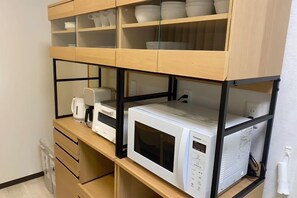 A kitchen with a microwave on a wooden shelf, a coffee maker, and a kettle. - Core Royal-Vacation Rental (Kyoto)