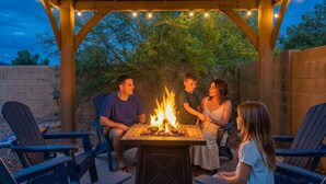 A covered outdoor seating area with a fire feature, surrounded by chairs and a table. - Desert Retreat | Pool | Fire Pit | Family Games (Surprise)