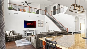 A spacious living room with a fireplace, a large TV, a staircase, and a dining area. - Desert Retreat | Pool | Fire Pit | Family Games (Surprise)