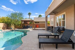 A pool area with a curved pool, lounge chairs, a covered seating area, and a patio with a table and chairs.