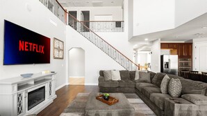 A modern living room with a sectional sofa, a flat-screen TV, a fireplace, and a staircase leading to an upper level. - Desert Retreat | Pool | Fire Pit | Family Games (Surprise)