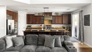 A modern kitchen with wooden cabinets, a granite countertop, and a bar area. - Desert Retreat | Pool | Fire Pit | Family Games (Surprise)