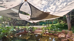 A garden with a pond, steps leading to a viewing area, and a shaded seating area. - Circle Goa (Anjuna)
