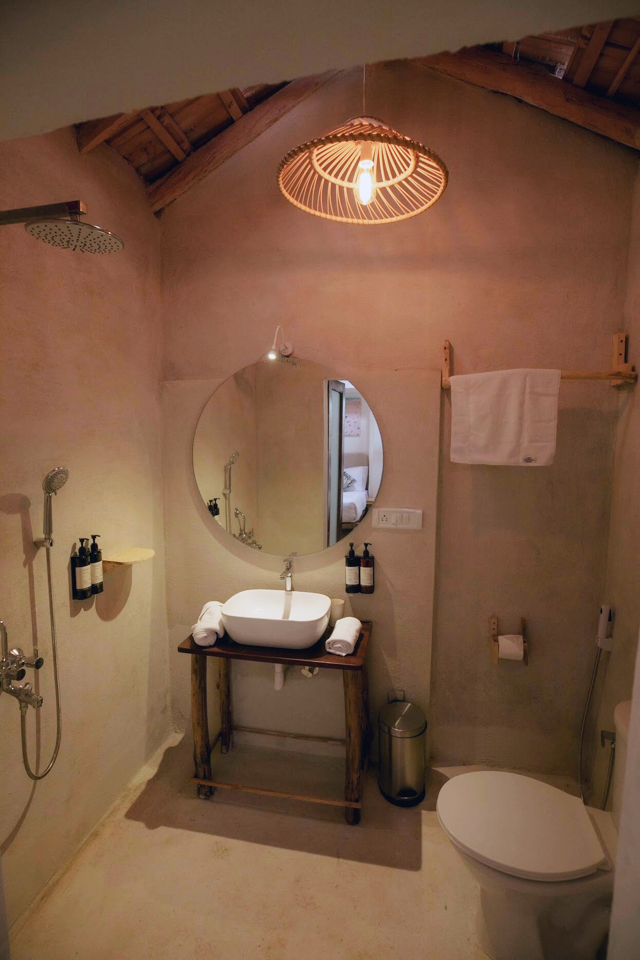 A bathroom with a wooden vanity, a round mirror, a shower, and a toilet.