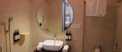 A bathroom with a wooden vanity, a round mirror, a shower, and a toilet.
