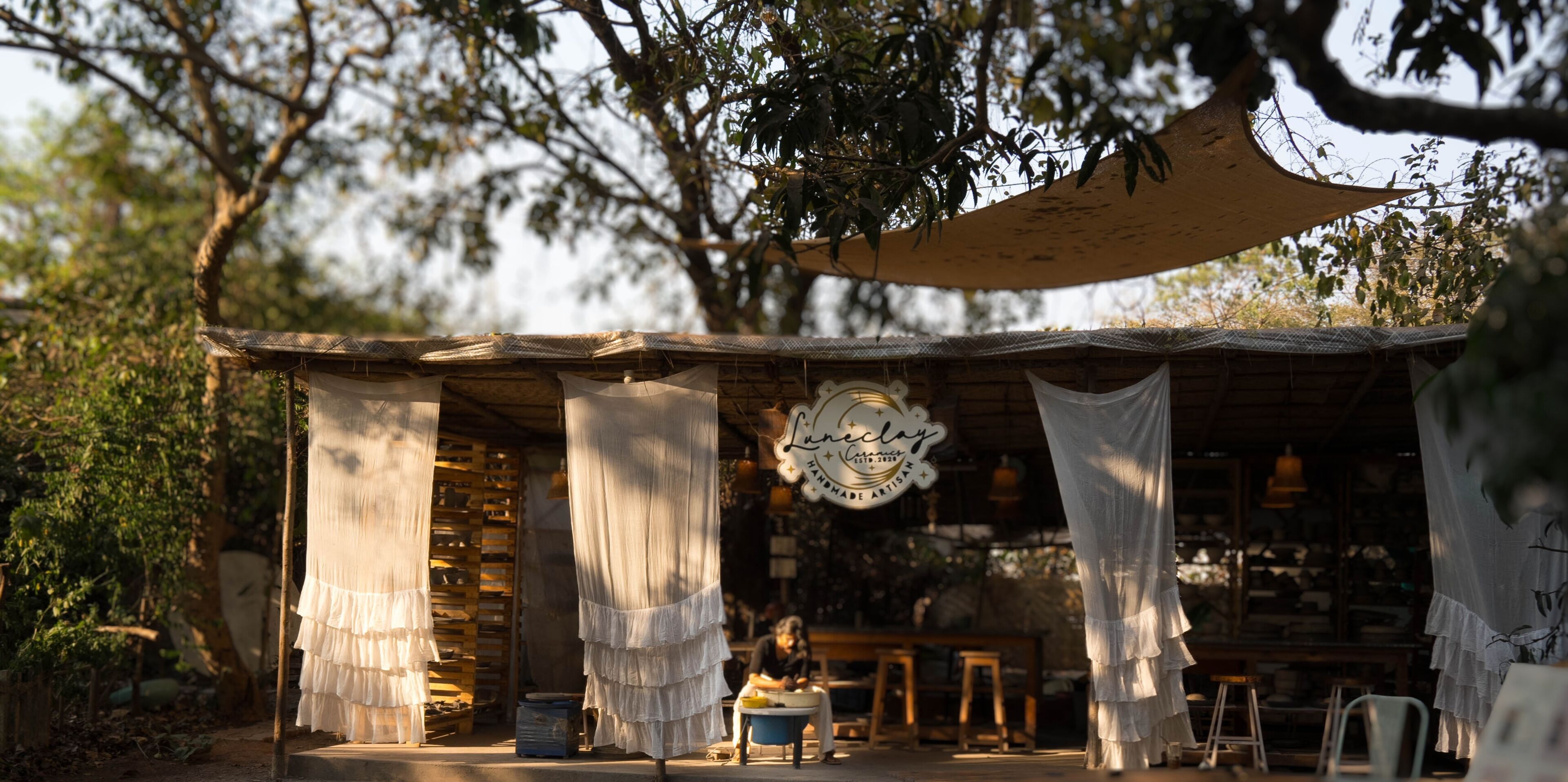 A rustic outdoor seating area with a canopy, wooden furniture, and hanging white curtains.
