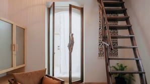 A modern living room with a glass coffee table, a brown sofa, a wooden ladder, and a staircase. - Circle Goa (Anjuna)