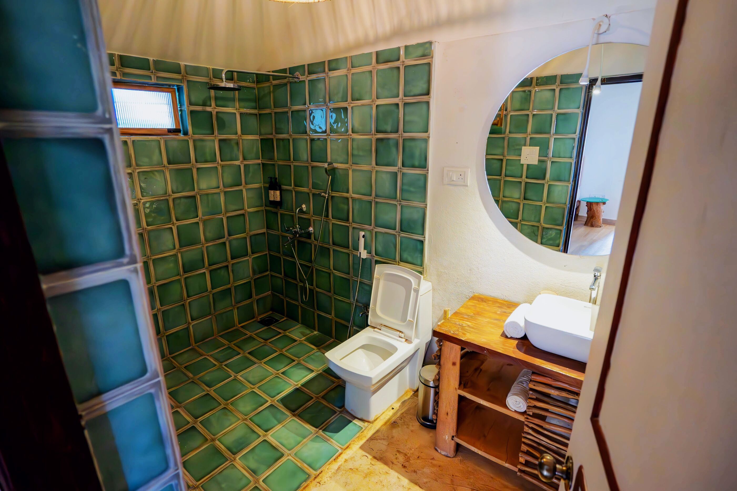 A bathroom with a green-tiled shower, a white toilet, and a wooden vanity with a sink.