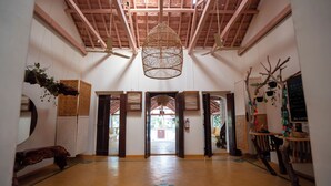 A spacious lobby with a high ceiling, wooden beams, and a hanging wicker chandelier. There are multiple doors leading to other areas, and the floor has a geometric pattern. - Circle Goa (Anjuna)