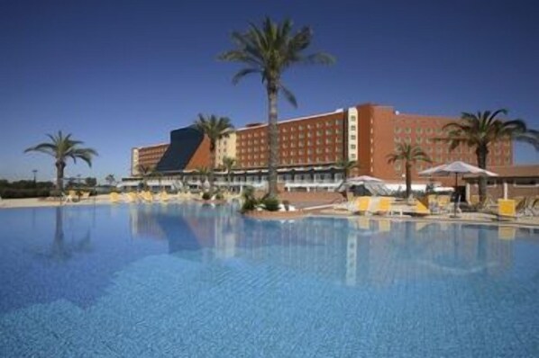 Ein Hotel mit großem Schwimmbad, Palmen und blauem Himmel.