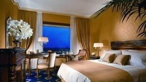 A hotel room with a bed, a desk, a chair, a lamp, and a view of the night sky. - Rome Marriott Park Hotel (Rome)